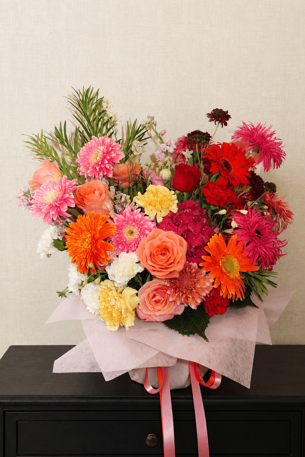 Colourful celebratory bouquet of coral, pink, orange, red and yellow flowers, wrapped in pale pink paper for “You Did It!”