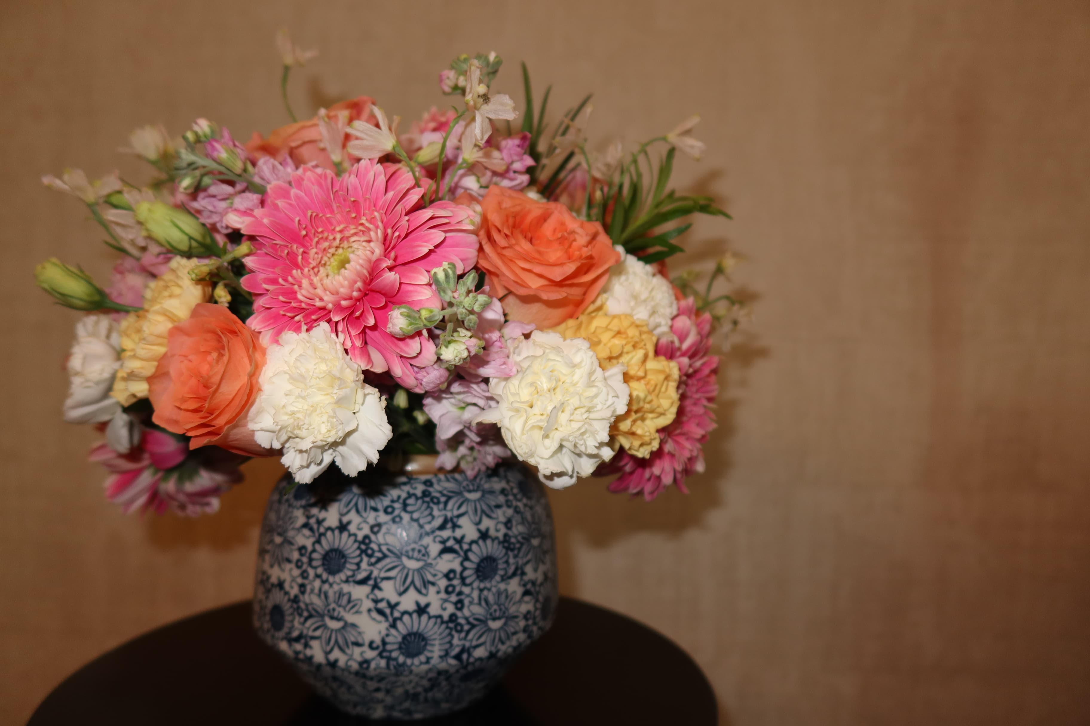 Pink, coral, cream and yellow flowers arranged in a blue-and-white patterned vase.