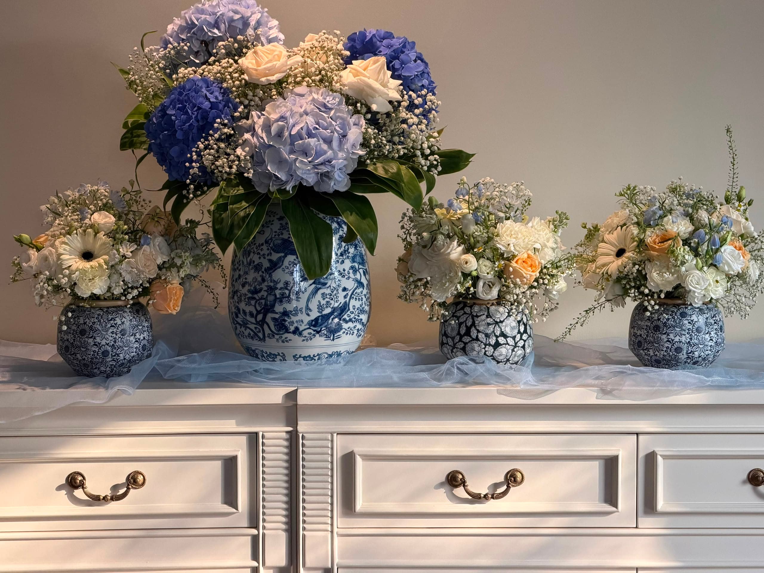 A collection of blue-and-white patterned vases filled with blue, white and peach seasonal flowers.