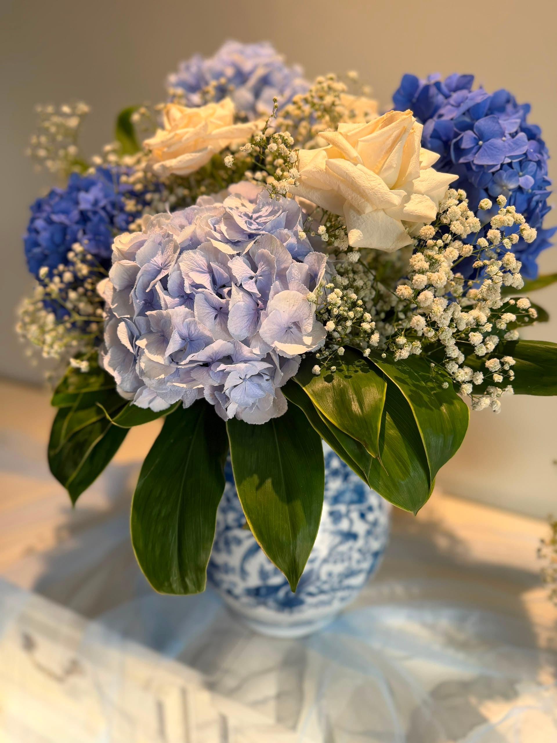 Large blue hydrangea and white rose arrangement in a blue-and-white patterned vase.