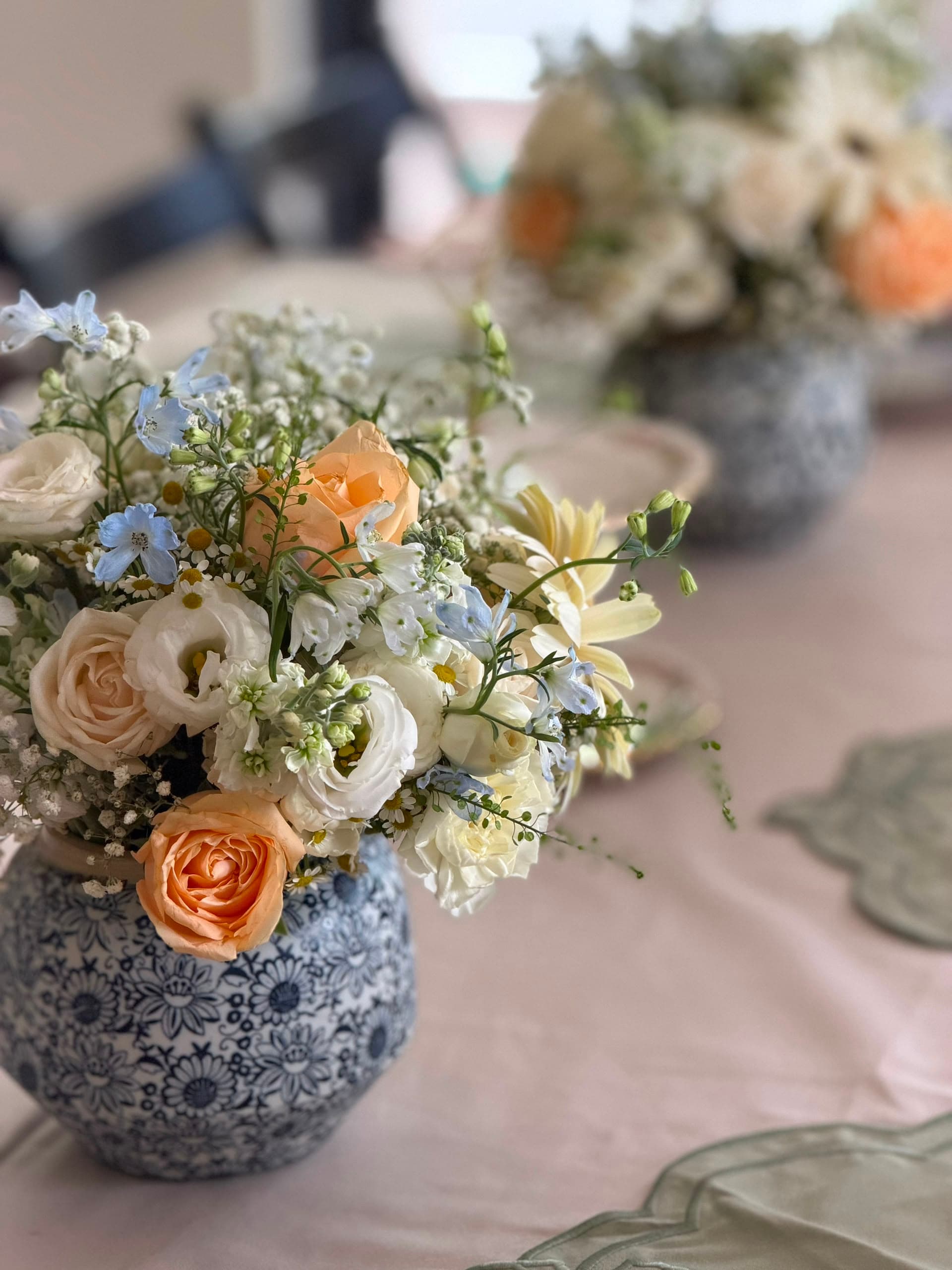 Small blue-and-white vase arrangement with peach roses, white flowers and soft blue accents.